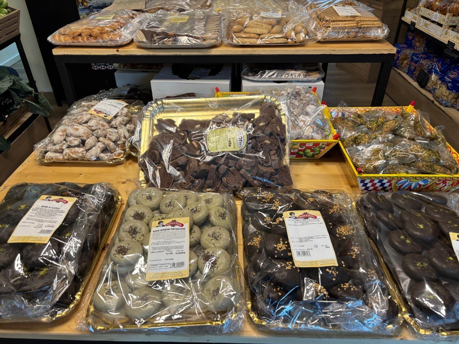 Rame di Napoli glassate al cioccolato e al pistacchio in vassoi dorati sul banco in legno di Tipicamente Siciliani
