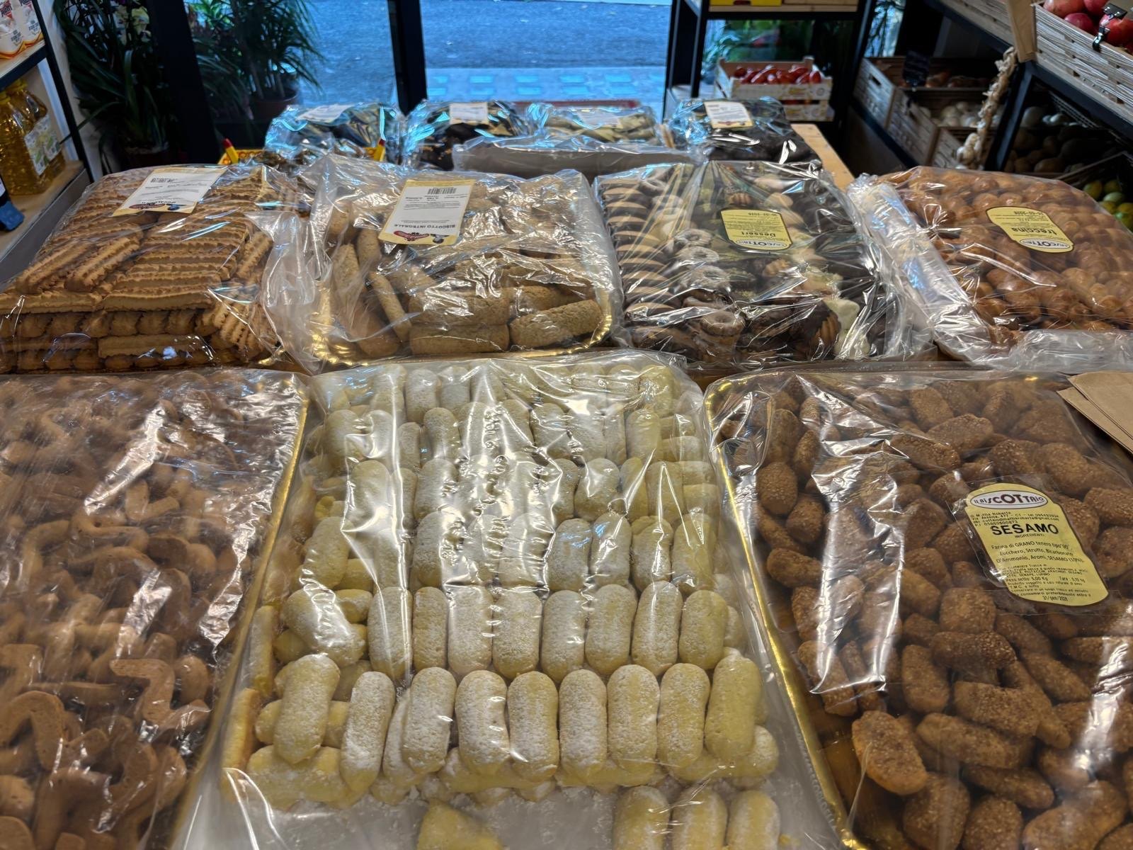 Vassoi incellofanati di biscotti assortiti su un banco, con dolcetti chiari zuccherati ed etichetta «Sesamo