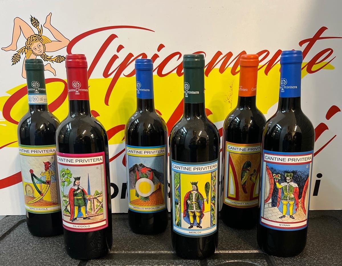 Sei bottiglie di vino Cantine Privitera con etichette di re e carretti siciliani davanti all'insegna Tipicamente Siciliani